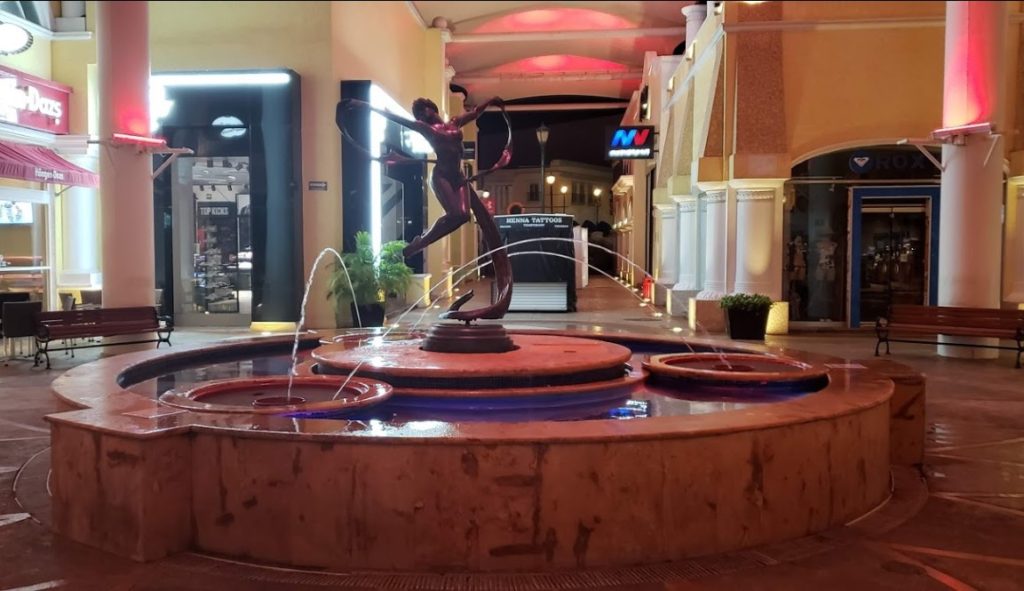 Water fountain with a scuplture of a woman in the middle located in La Isla Shopping Village Cancun surrounded by clothing and ice cream stores