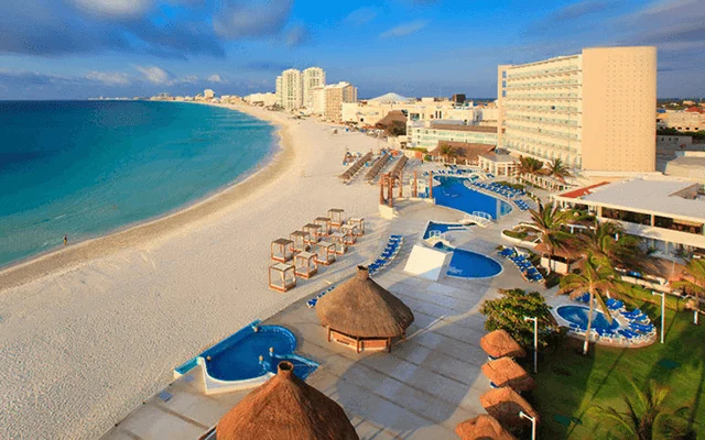 View of Cancun Hotel Zone beach with Beachfront Resorts, pools, calmed sea and bali beds.