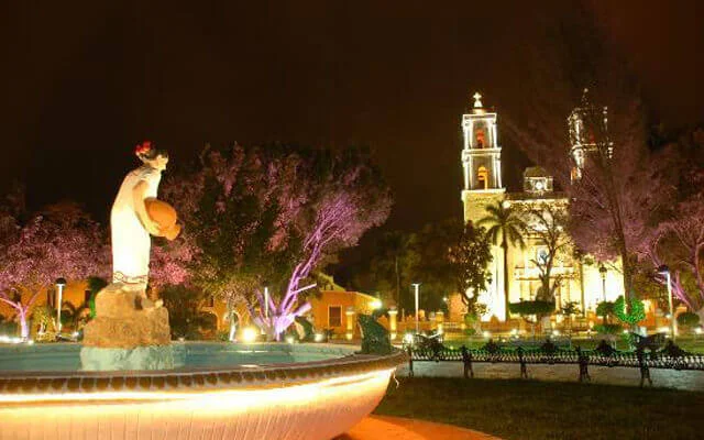 Sculpture and church at a square of Valladolid during night. One of the destinations available for Cancun Airport Transportation