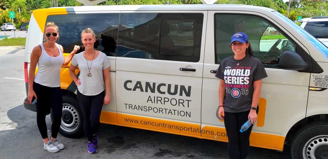 Group of happy customers composed by three women smiling in front of a van labeled by Cancun Airport Transportation