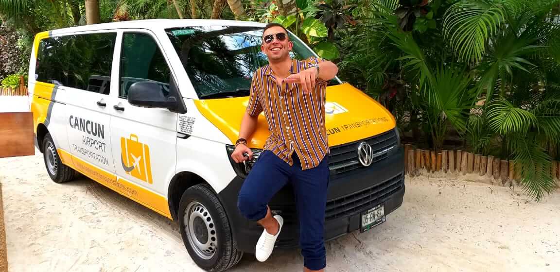Happy customer smiling and pointing to the camera lens with a Cancun Airport Transportation van on the background