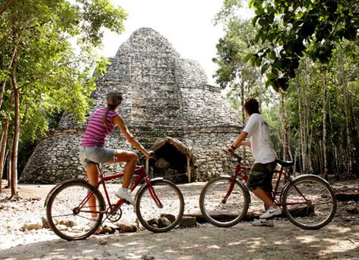 Two persons riding bicicle in front of Nohoch Mul, Coba. One of the destinations available for Cancun Airport Transportation