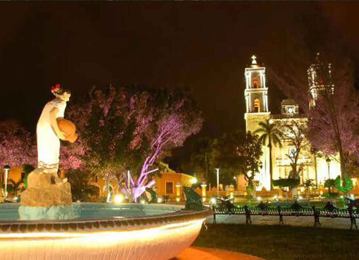 Sculpture and church at a square of Valladolid during night. One of the destinations available for Cancun Airport Transportation